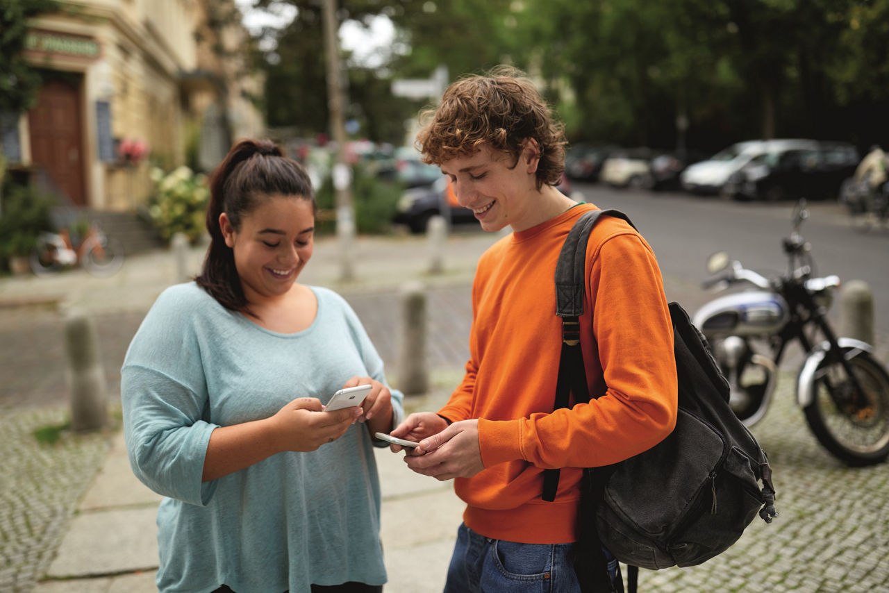 Konten, Karten und Apps - Junge und Mädchen stehen zusammen auf der Straße und schauen ins Smartphone