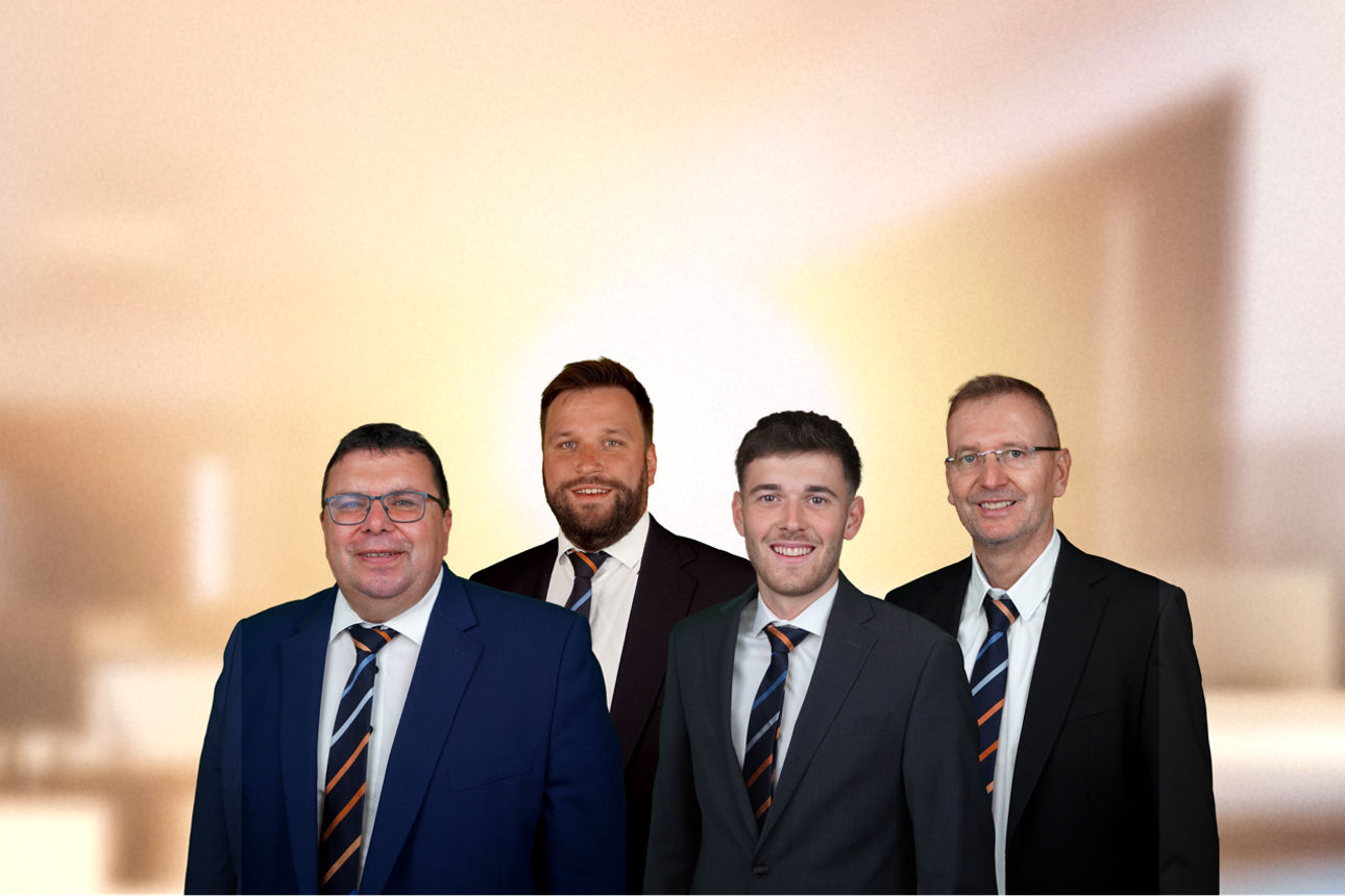 Vier Baufinanzierungsberater der VR MiO stehten mit Krawatte in einem Büro