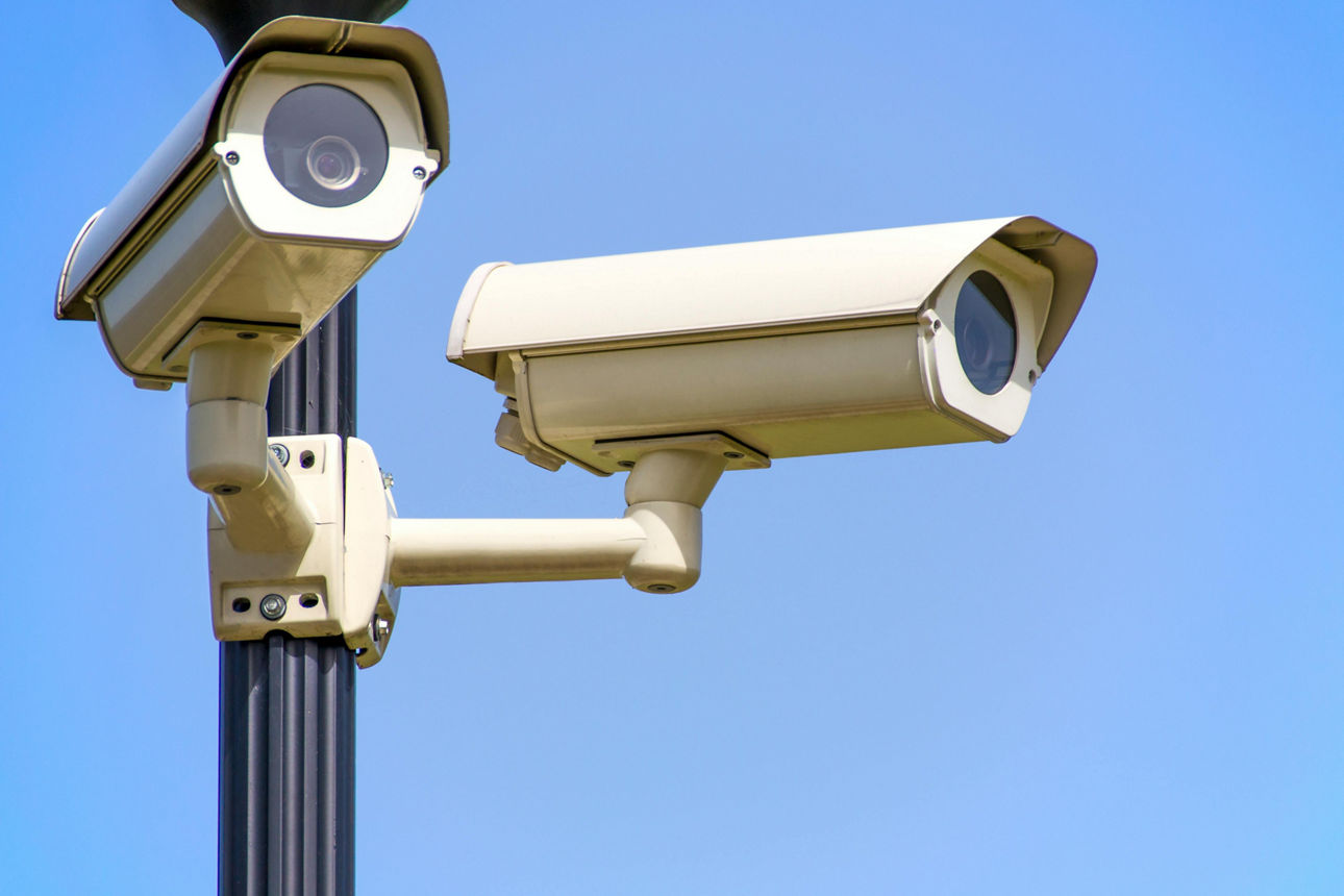weisse-2-cctv-kamera-auf-schwarzem-pfosten-unter-blauen-himmel