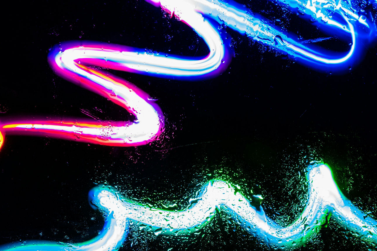 Abstrakte Neonlinien in verschiedenen Farben auf schwarzem Hintergrund mit Reflexionen und Tropfen.