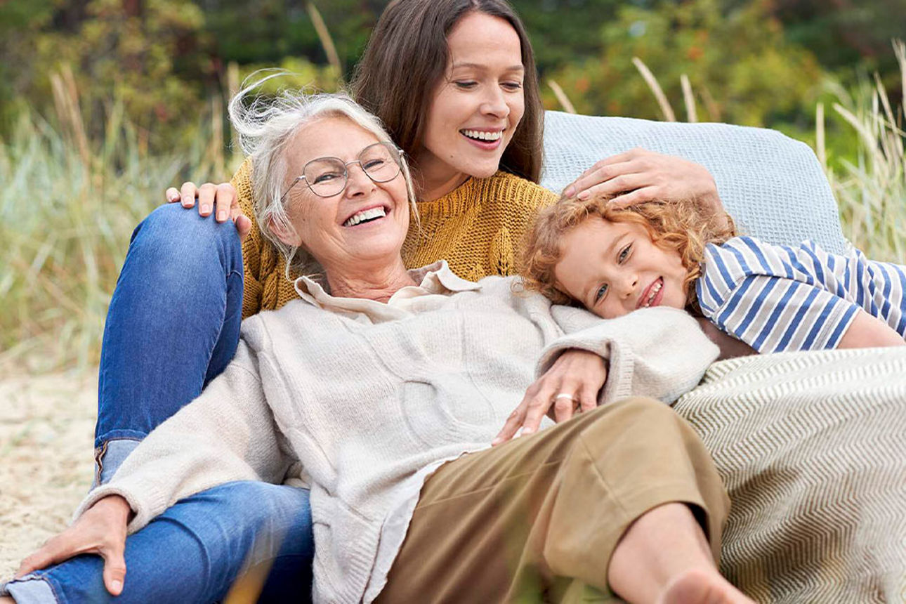 Eine Großmutter, Mutter und Tochter liegen gemeinsam auf einer Decke am Strand.