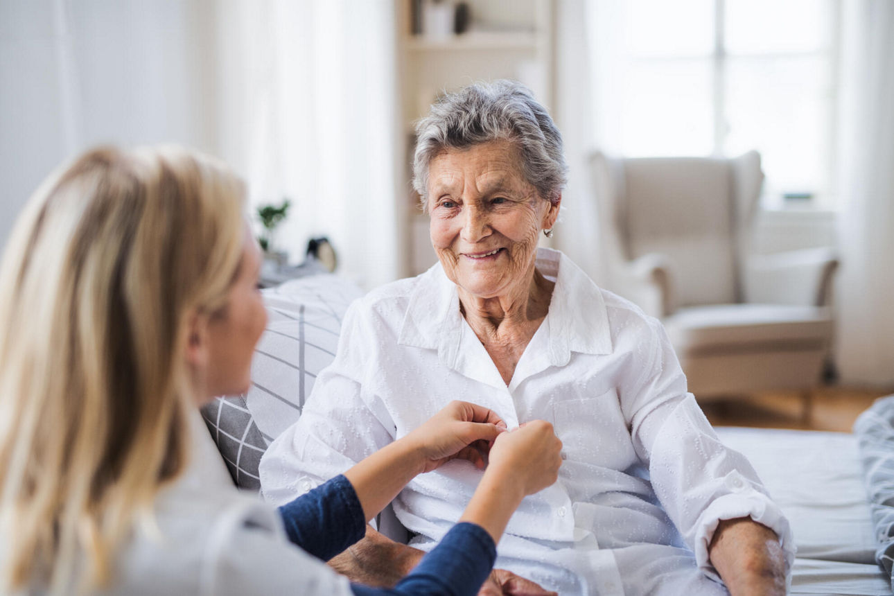 Pflegekraft hilft einer Seniorin beim Anziehen