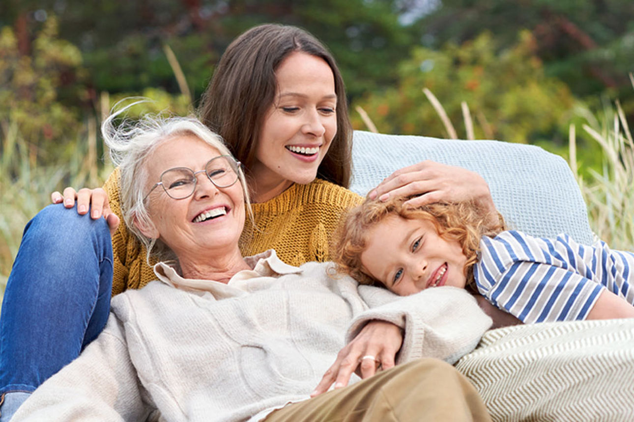 Mutter, Oma und Kind liegen draußen in der Natur 
