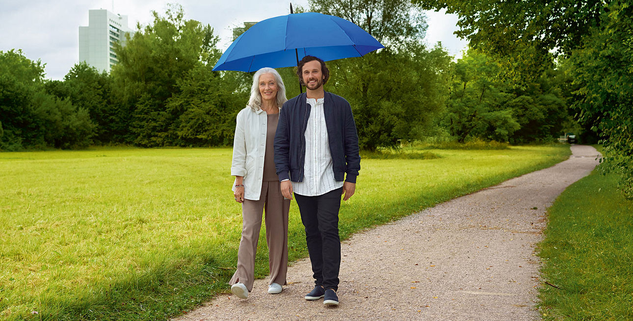 Mann und Frau unter einem blauen Regenschirm stehen auf einem Feldweg