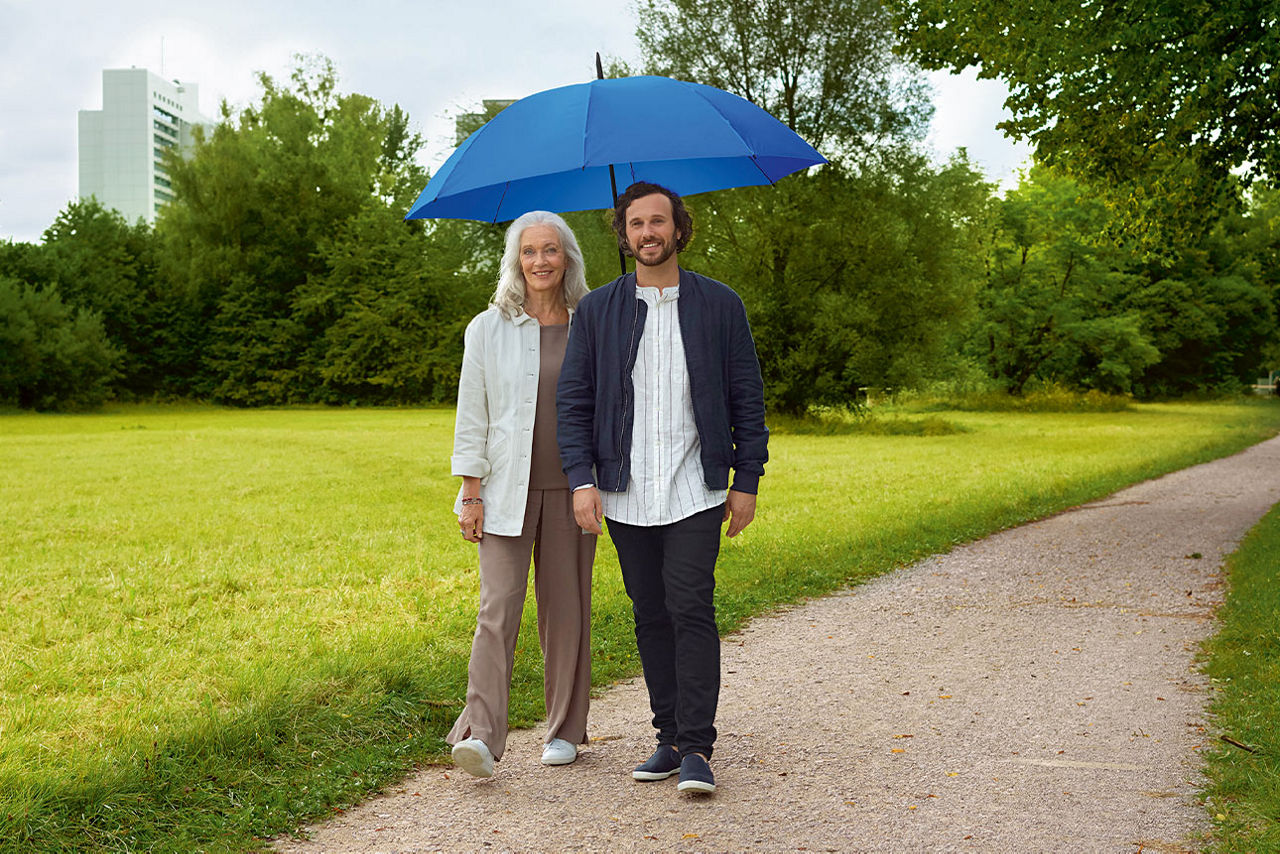 Mann und Frau unter einem blauen Regenschirm stehen auf einem Feldweg