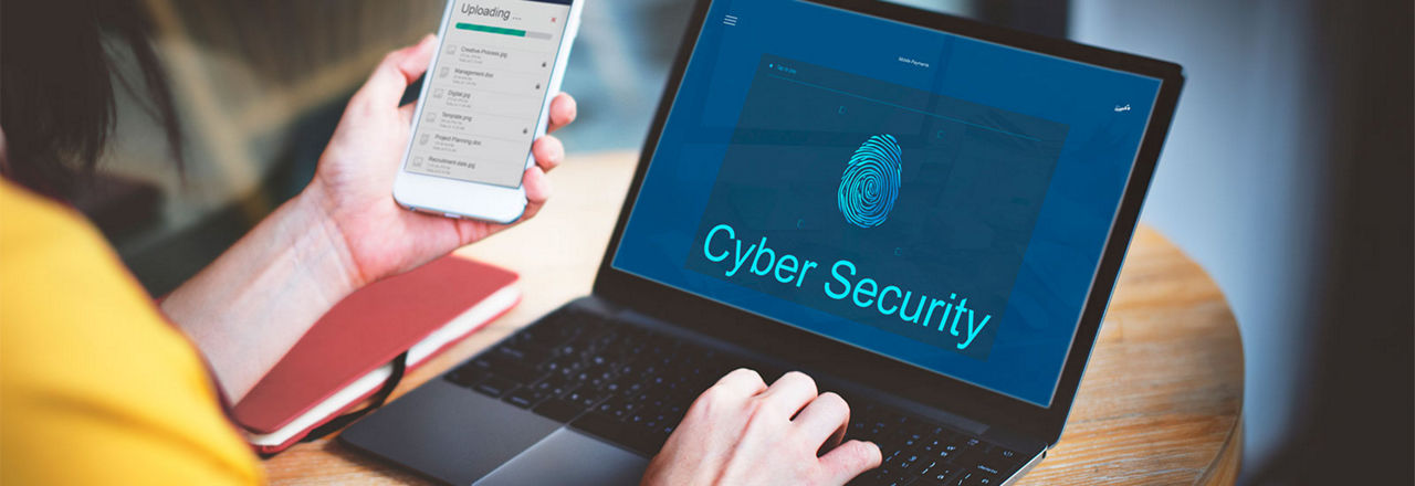 Frau hält Smartphone in der Hand und sitzt vor Laptop, wo Cyber Security drauf steht.