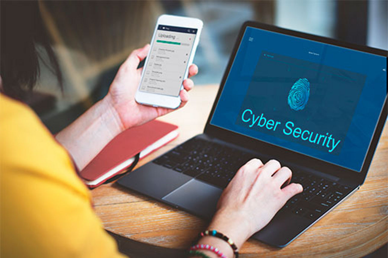 Person hält Smartphone mit Ladeanzeige und bedient Laptop mit Anzeige eines Fingerabdrucks und dem Text 'Cyber Security'