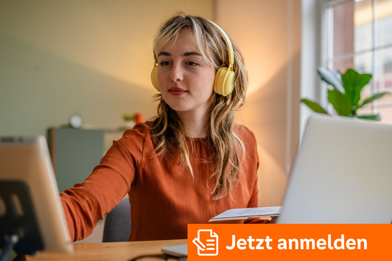 Person arbeitet am Schreibtisch mit Laptop, Tablet und Unterlagen und trägt gelbe Kopfhörer.