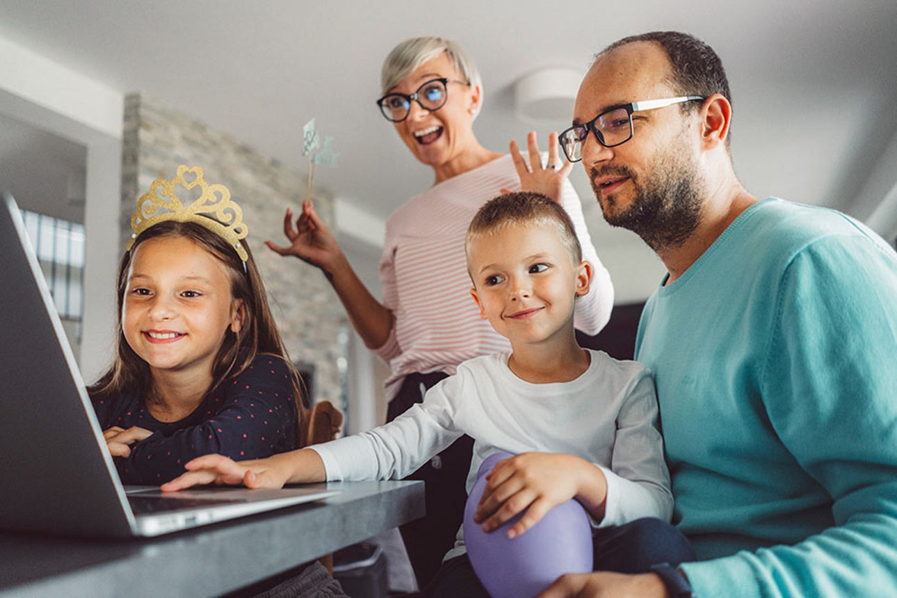 Eine vierköpfige Familie sitzt vor einem Laptop. Das junge Mädchen trägt eine Krone