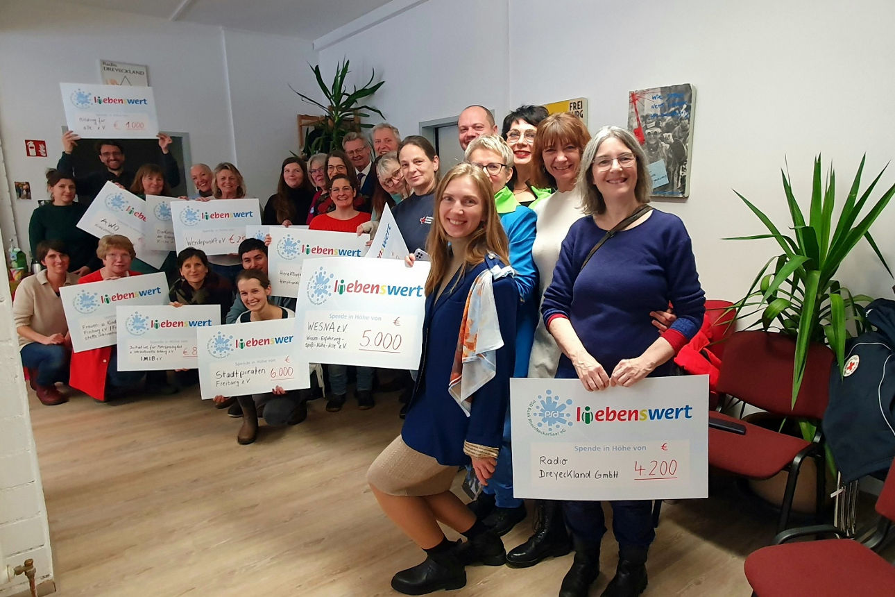 Eine Gruppe von Menschen steht zusammen und hält Spendenschecks in den Händen.