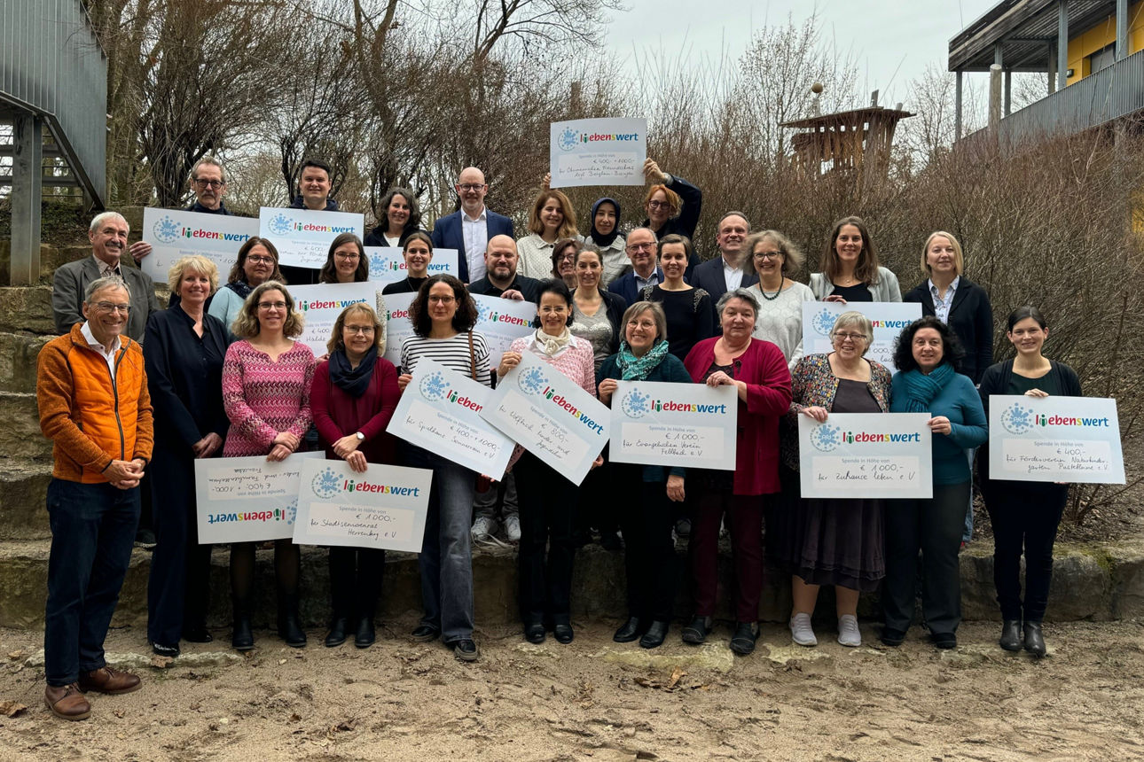 Eine Gruppe von Menschen steht zusammen und hält Spendenschecks in den Händen.