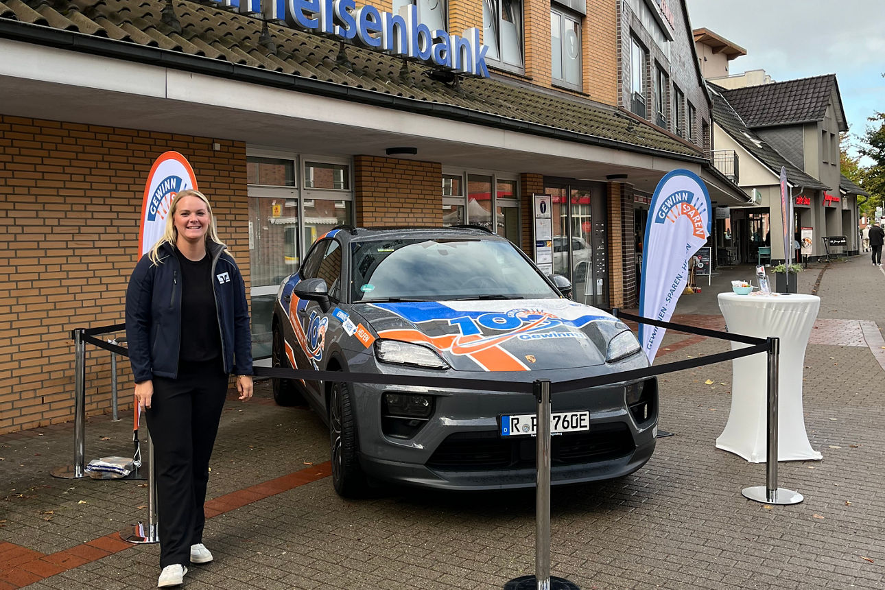 Eine junge Frau steht draußen vor der Raiffeisenbank in Bargteheide mit einem bedruckten Porsche Macan.