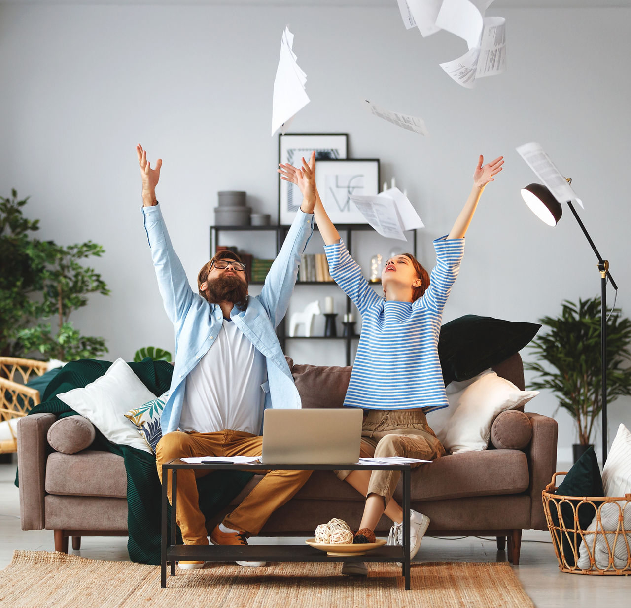 Paar sitzt auf der Couch und wirft Papierblätter in die Luft