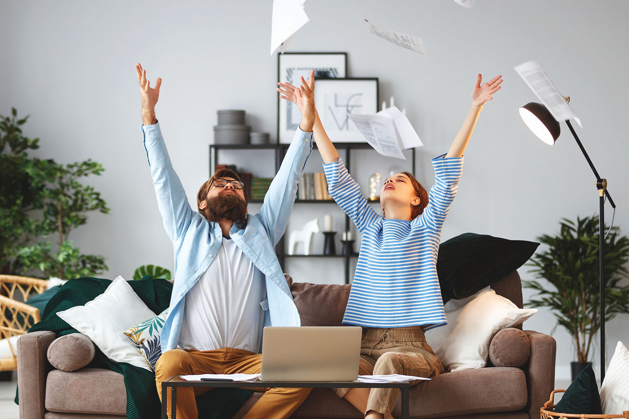 Paar sitzt auf der Couch und wirft Papierblätter in die Luft