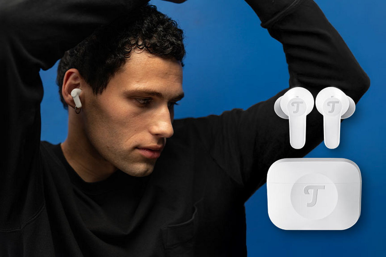 Ein Mann mit schwarzem Oberteil trägt weiße kabellose Teufel In-Ear-Kopfhörer vor blauer Wand.