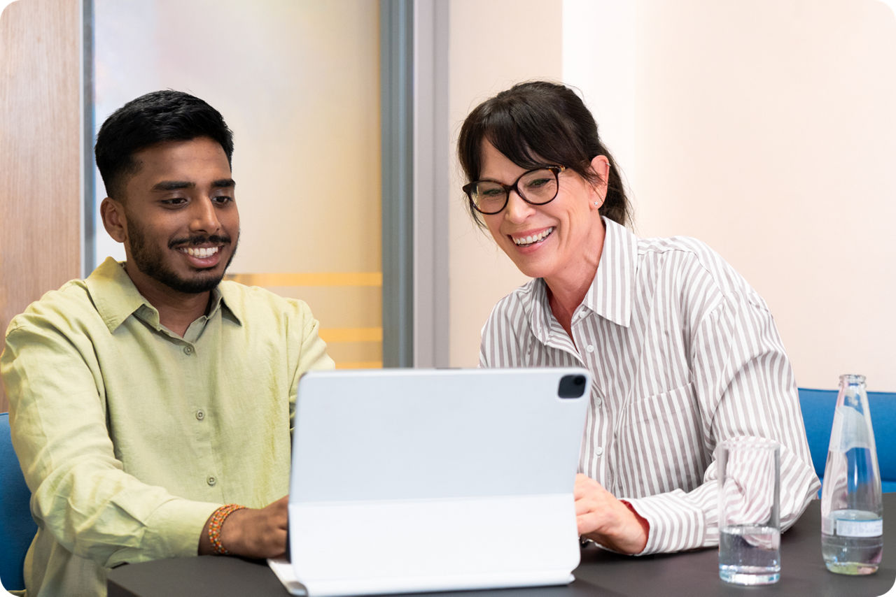 Eine Ausbilderin und ein Student sitzen vor einem Laptop und lächeln