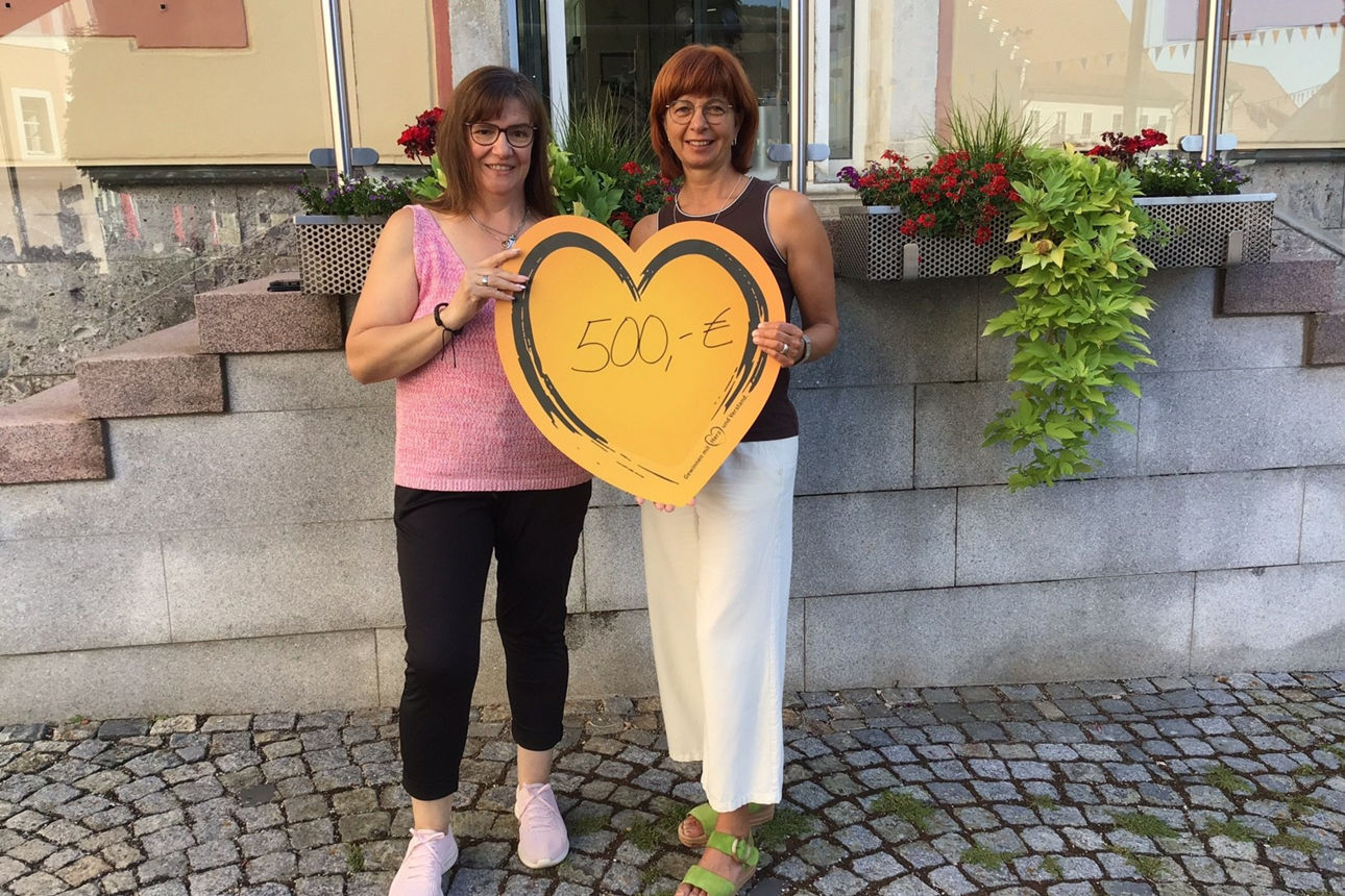 zwei Frauen halten ein Herz mit dem Betrag  500 € in die Höhe
