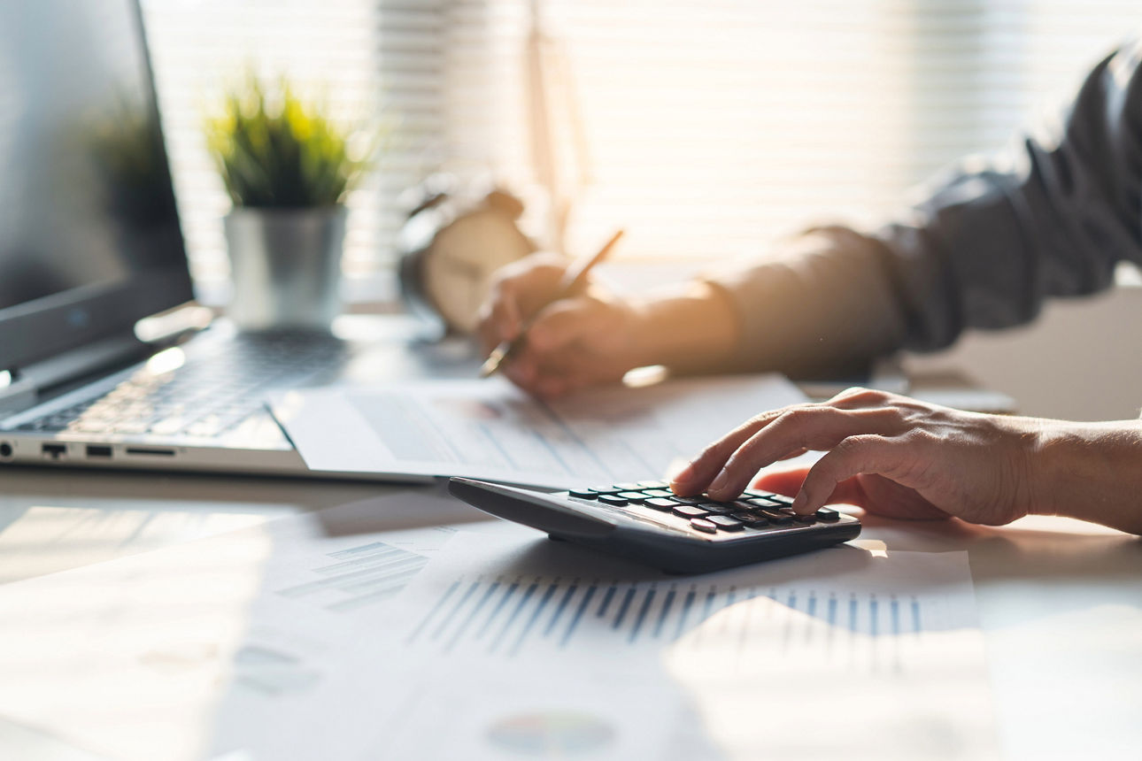 Person sitzt am Schreibtisch und bedient einen Taschenrechner