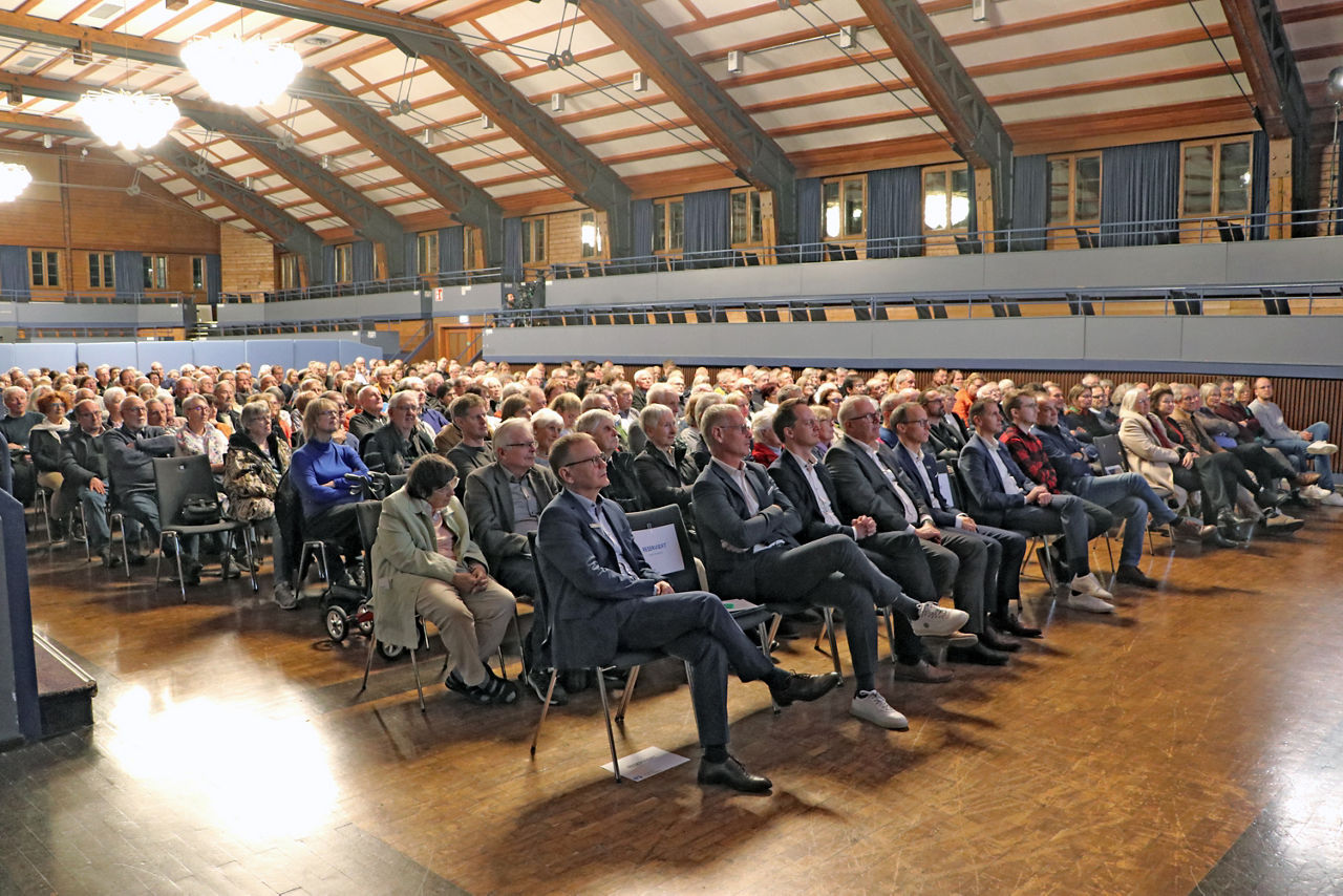 Personen sitzen in einer großen Halle in Reihen und schauen Richtung Bühne beim MitgliederForum.