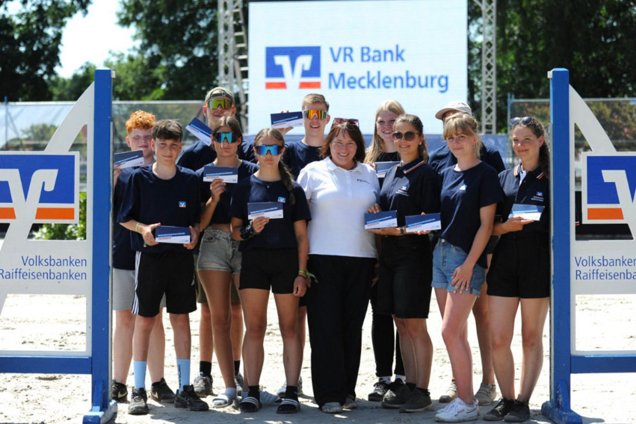 Elf Jugendliche stehen mit einer Bank-Mitarbeiterin auf dem Reitplatz in Redefin