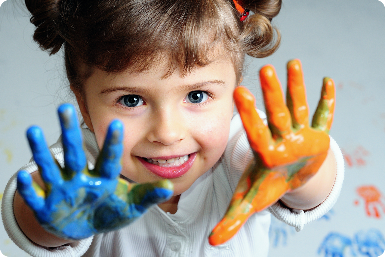 Ein Mädchen hat sich mit Fingerfarbe orange-blaue Hände bemalt