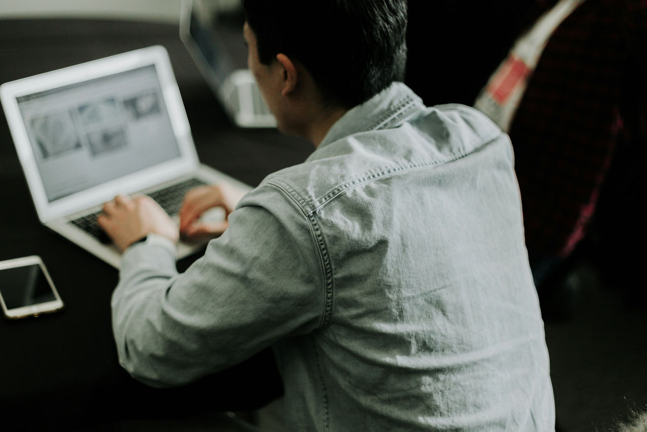 Junger Mann sitzt mit seinem Laptop an einem Tisch