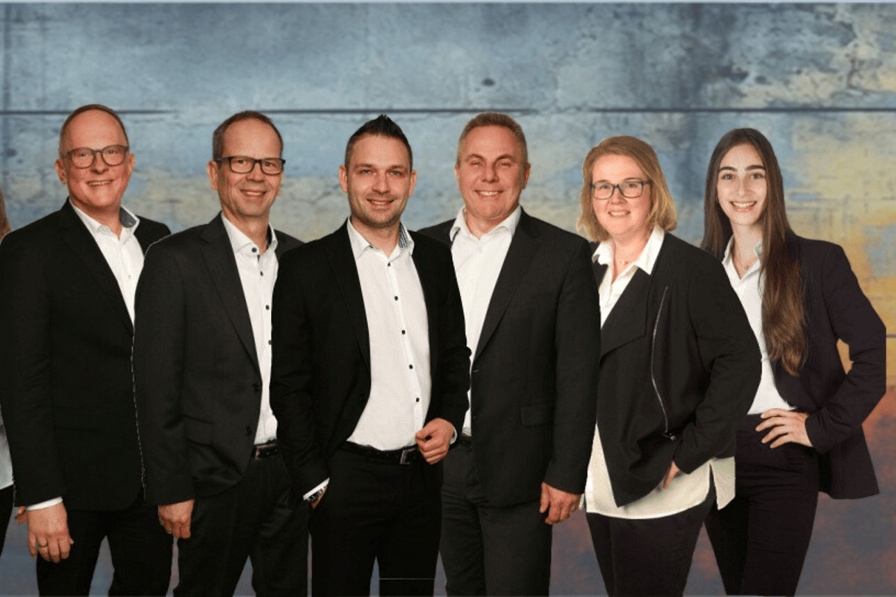 Gruppe elegant gekleideter Personen posiert vor einem farbigen Hintergrund in Business-Atmosphäre.