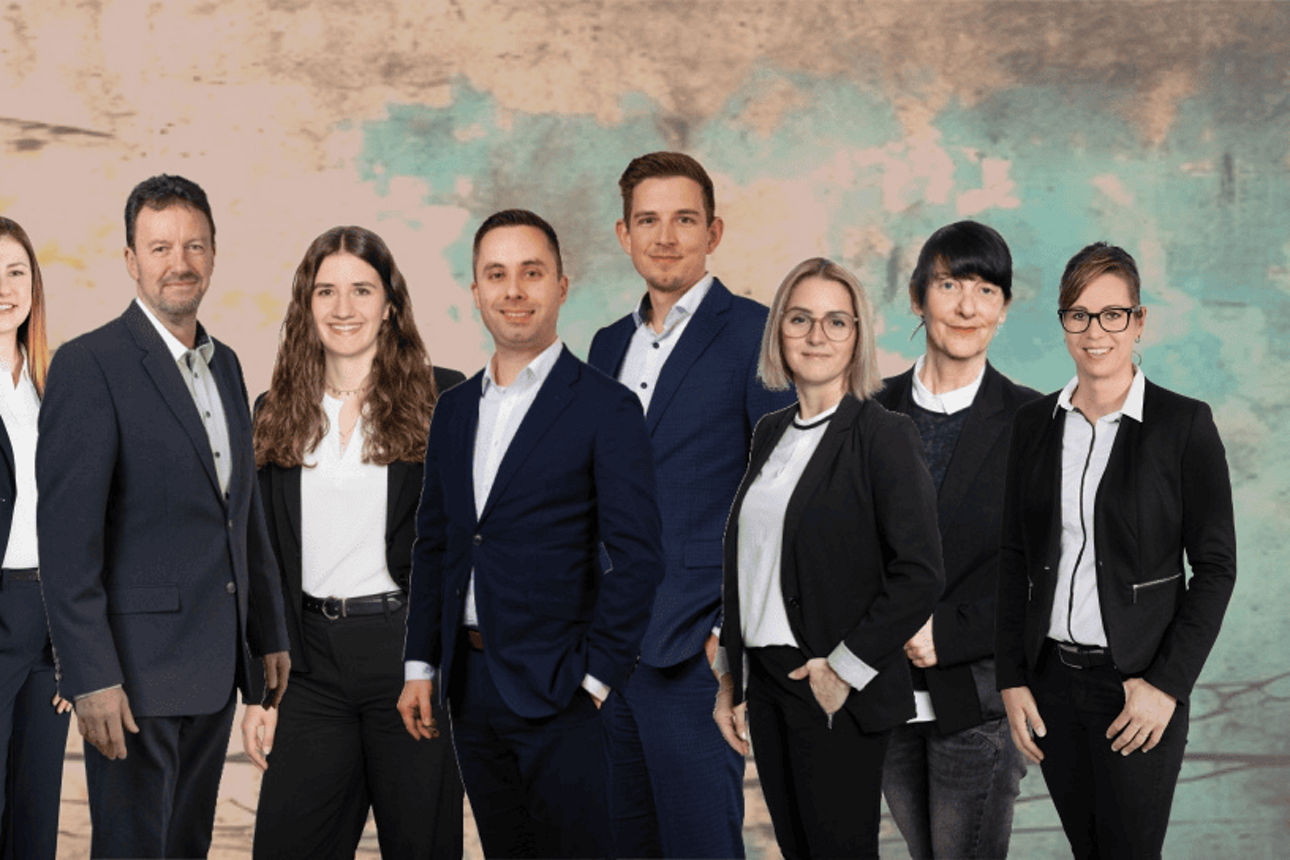 Gruppe elegant gekleideter Personen posiert vor einem farbigen Hintergrund in Business-Atmosphäre.