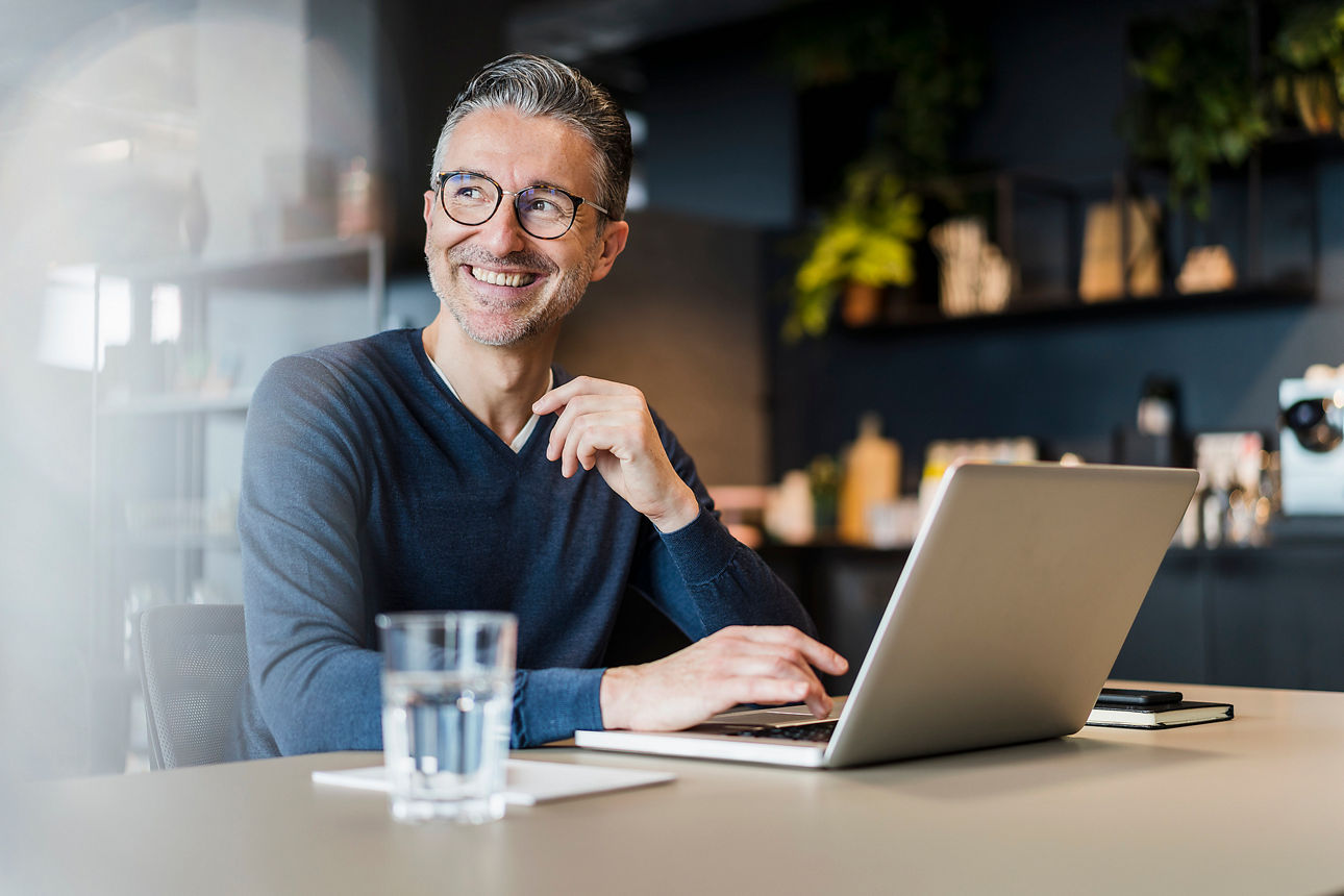 Mann sitzt mit Laptop am Schreibtisch.