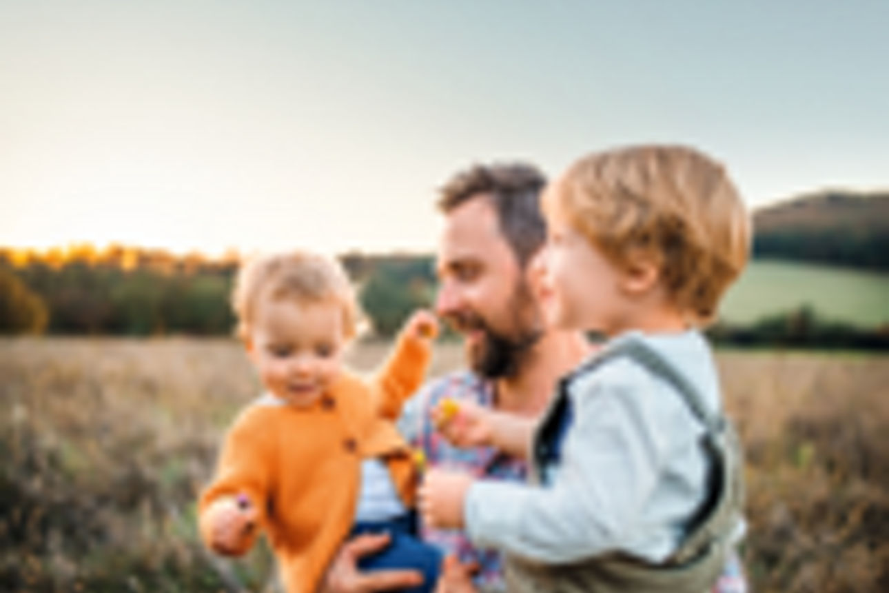 Vater mit zwei Kleinkindern auf den Armen steht auf einem Feld