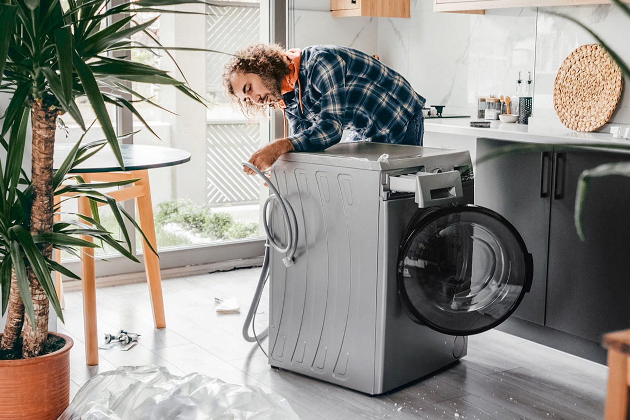 Junger Mann überprüft in der Küche den Wasserschlauch der Waschmaschine