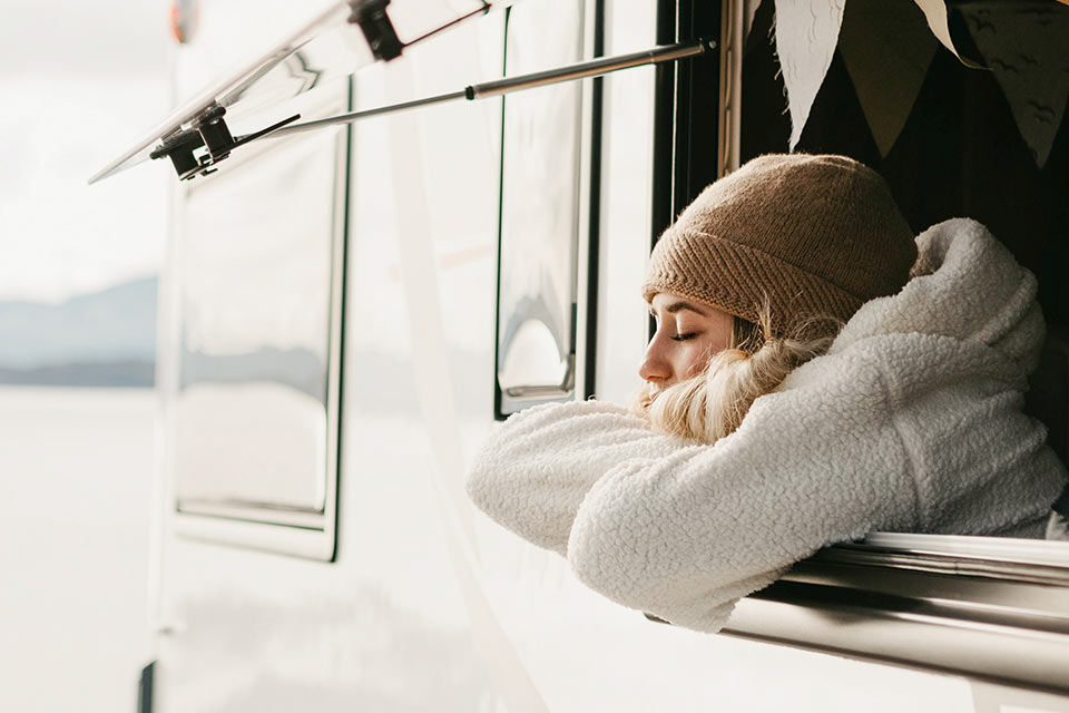 Eine Frau sitzt mit geschlossenen Aufgen am Fenster eines Campervans
