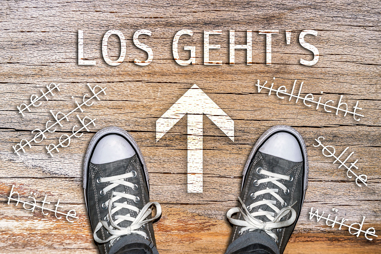 Aufschrift Los gehts, darunter zwei Schuhe und ein Pfeil in der Mitte auf hölzernem Hintergrund.