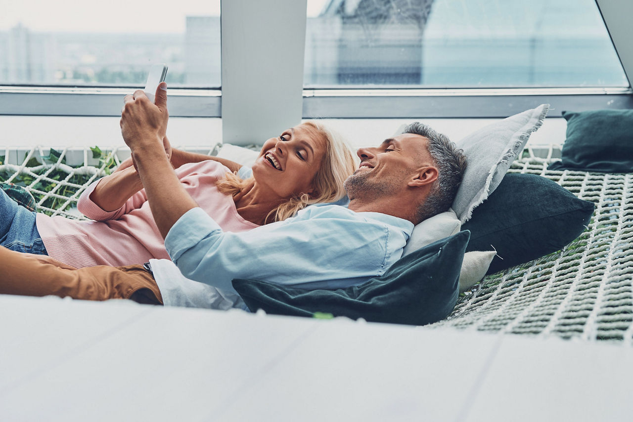 Mann und Frau liegen auf der Couch und schauen auf das Handy