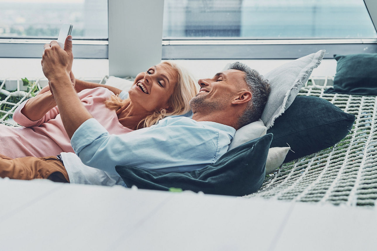 Paar liegt relaxt auf einer Netzhängematte und schaut gemeinsam in ein Smartphone