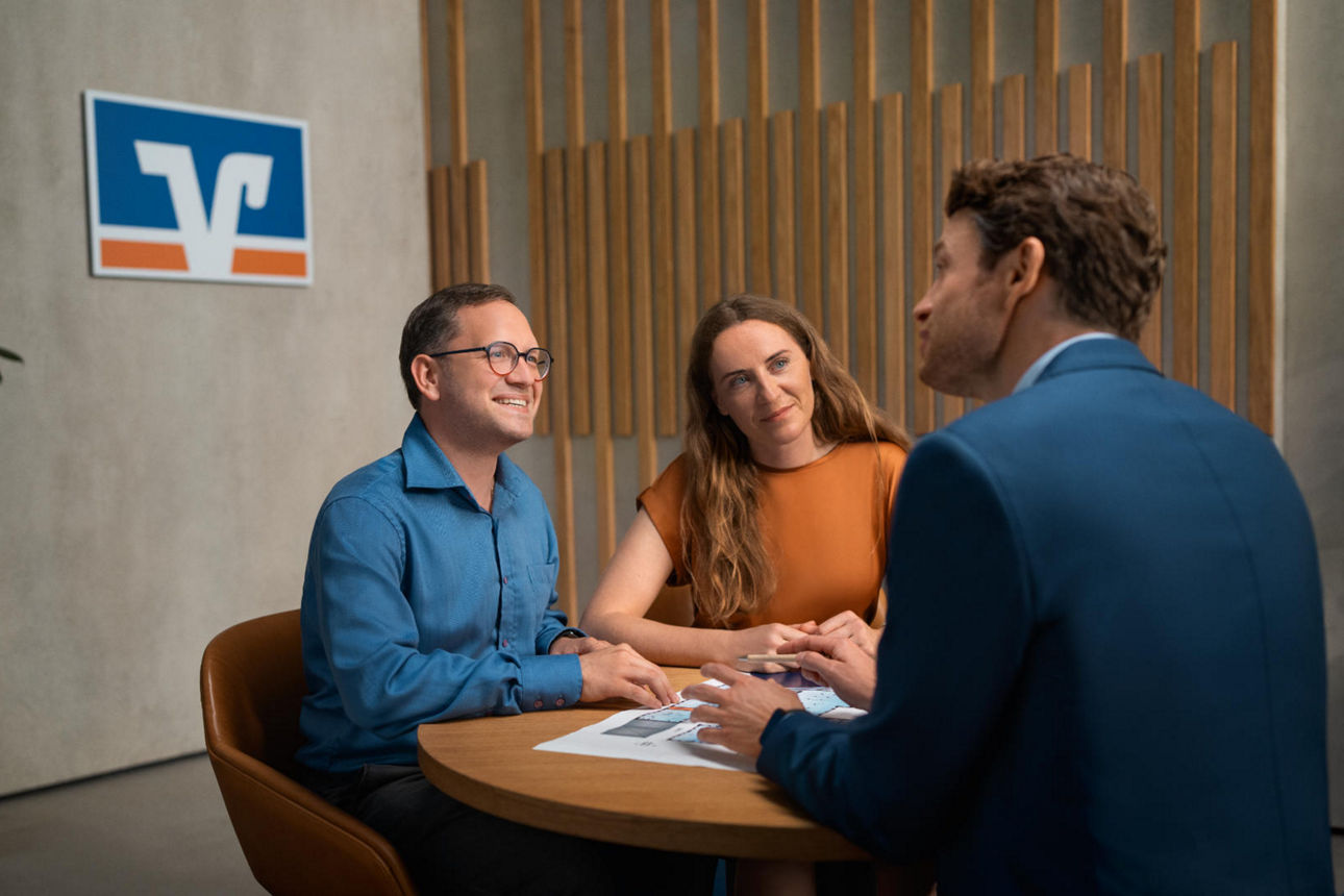 Berater mit zwei Kunden im Beratungsgespräch sitzen am Tisch