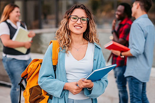 Junge Frau und andere junge Leute mit Büchern und Unterlagen auf einem Hochschul-Campus