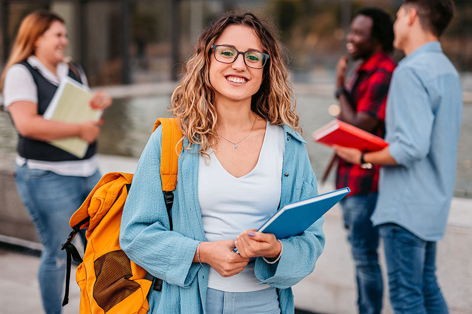 Junge Frau und andere junge Leute mit Büchern und Unterlagen auf einem Hochschul-Campus