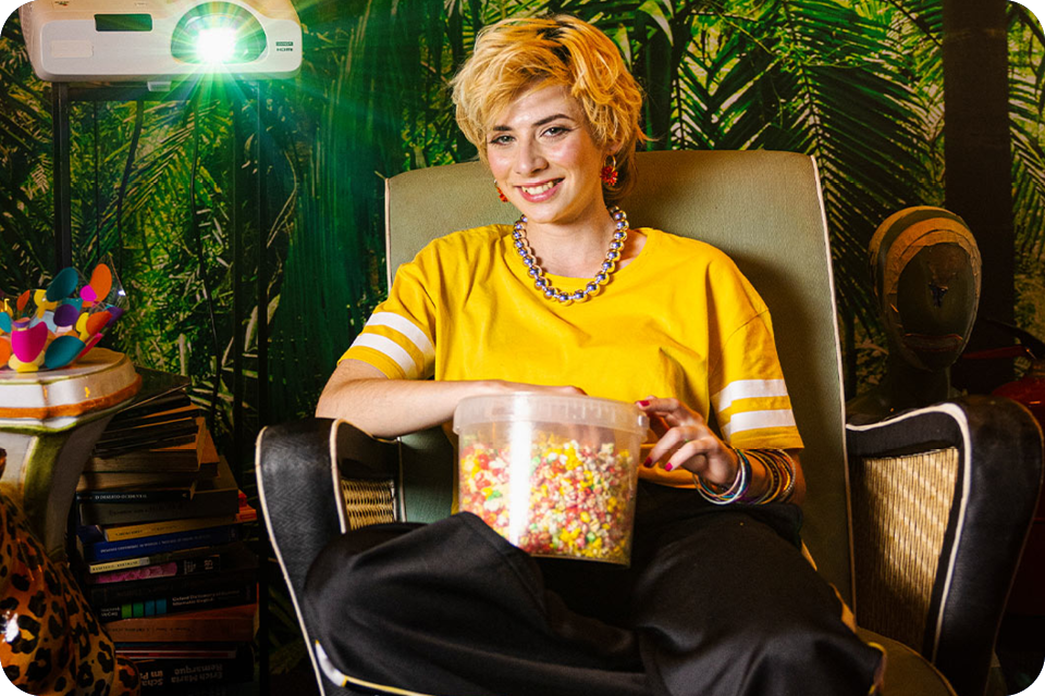 Person mit Popcorn im Sessel vor tropischer Pflanzenkulisse.