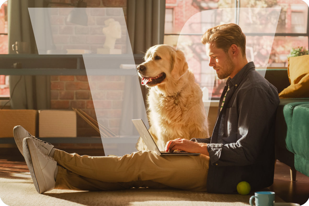 Mann sitzt neben Hund im Wohnzimmer auf dem Boden und schreibt am Laptop