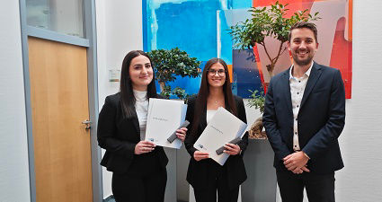 Zwei ausgelernte Auszubildende mit einem Herren und Zeugnissen. 