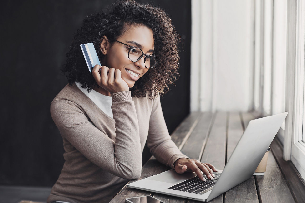 Eine Frau hält ihre Girocard in der hand und blickt auf das Laptop. 
