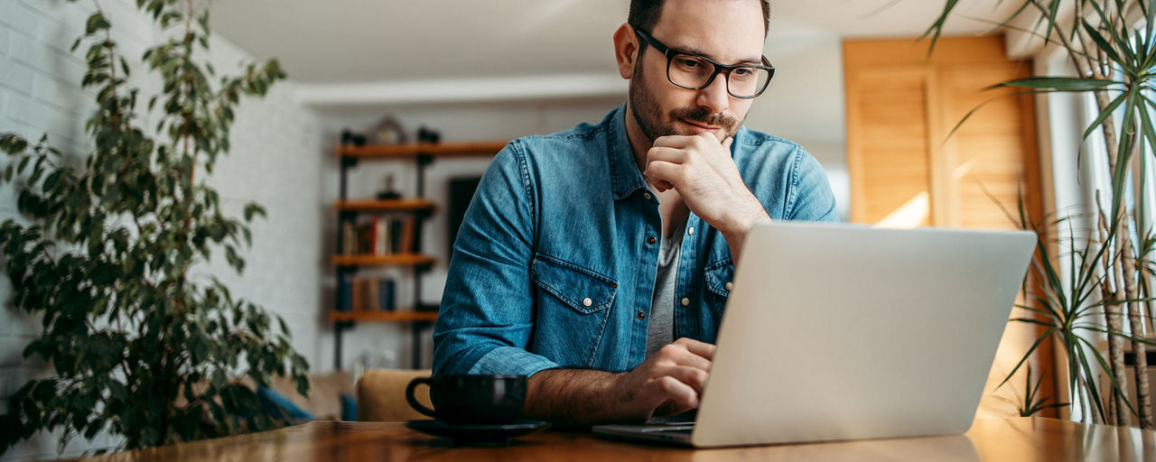Ein Mann sitzt am Tisch und schaut auf seinen Laptop