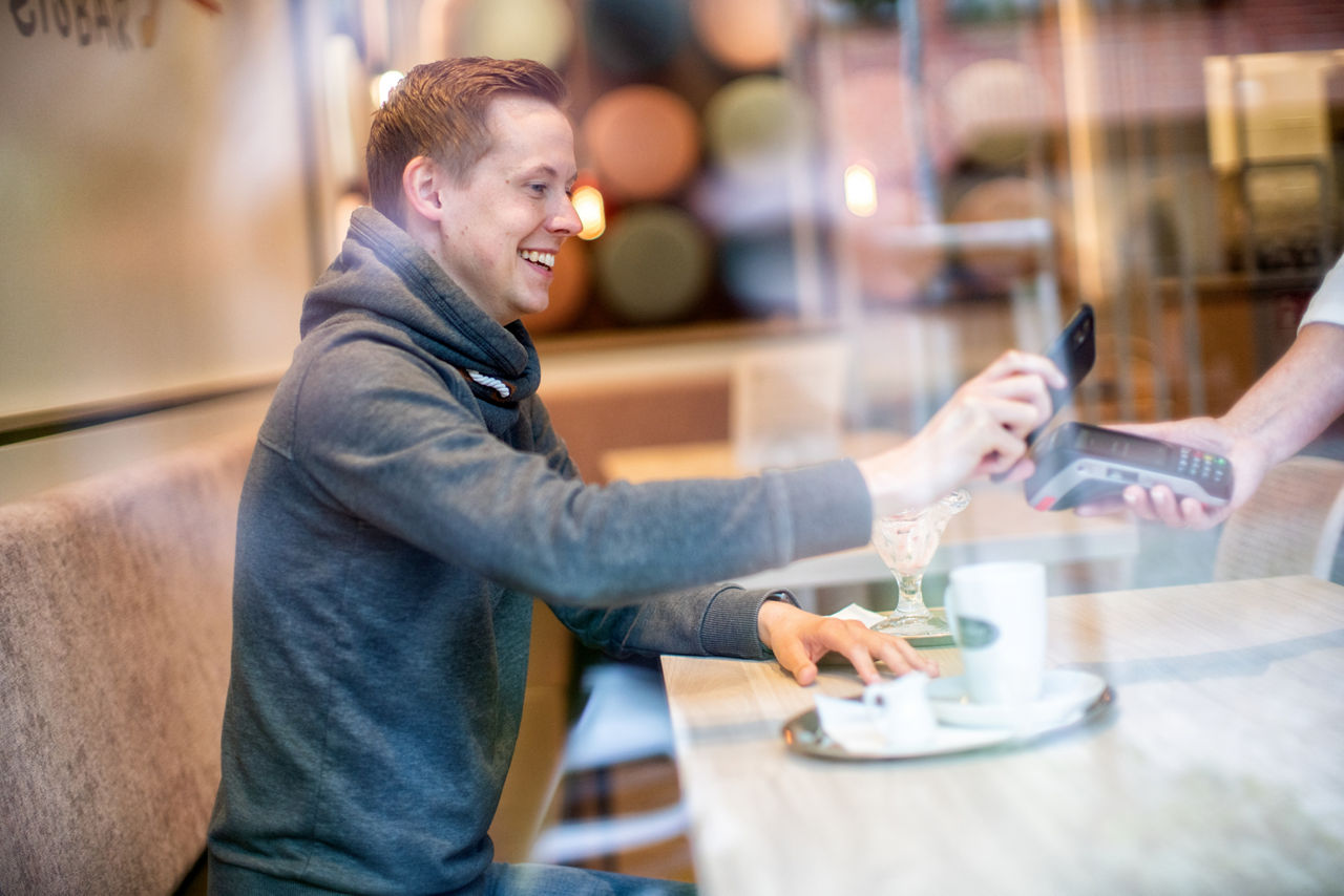 Mann bezahlt im Eiscafe bargeldlos mit seinem Smartphone