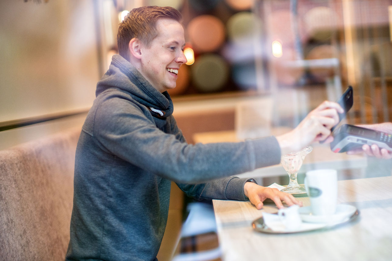 Mann bezahlt im Eiscafe bargeldlos mit seinem Smartphone