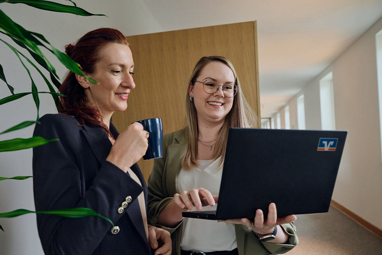 Zwei Frauen eine mit Kaffeetasse eine mit Laptop