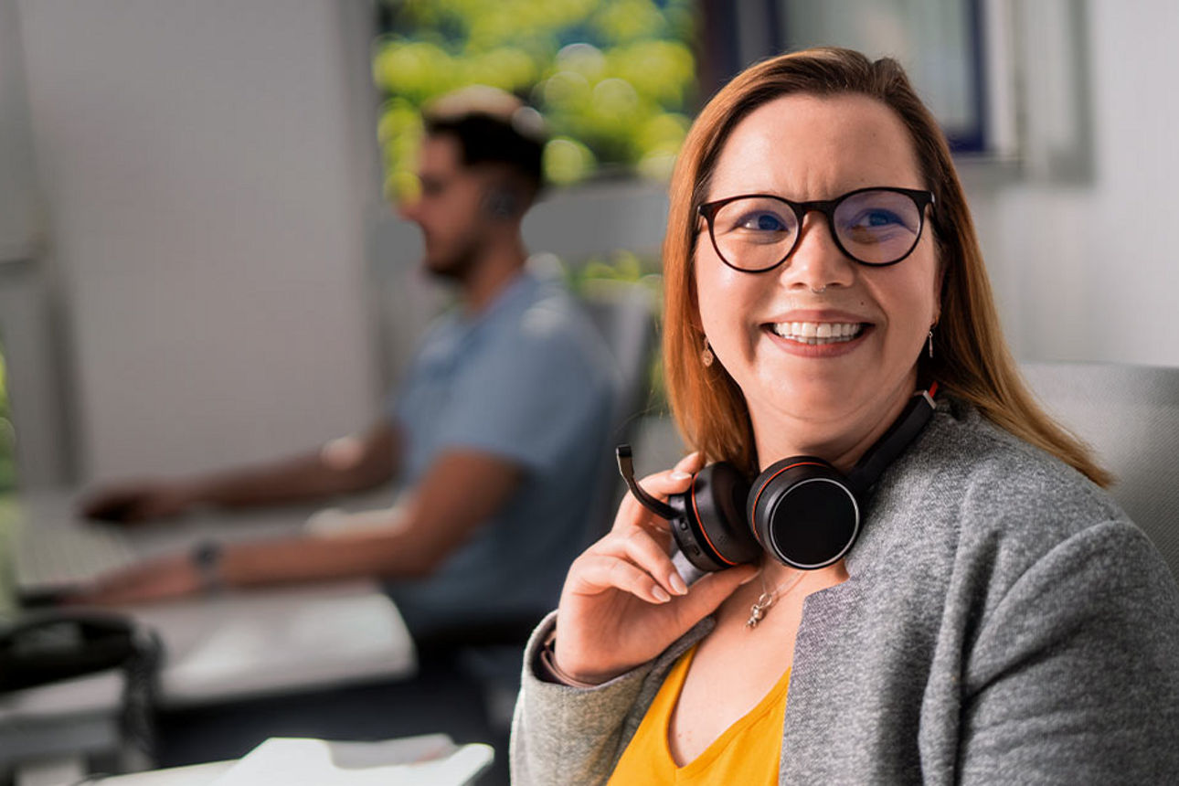 Eine Frau mit Headset sitzt lächelnd an ihrem Arbeitsplatz