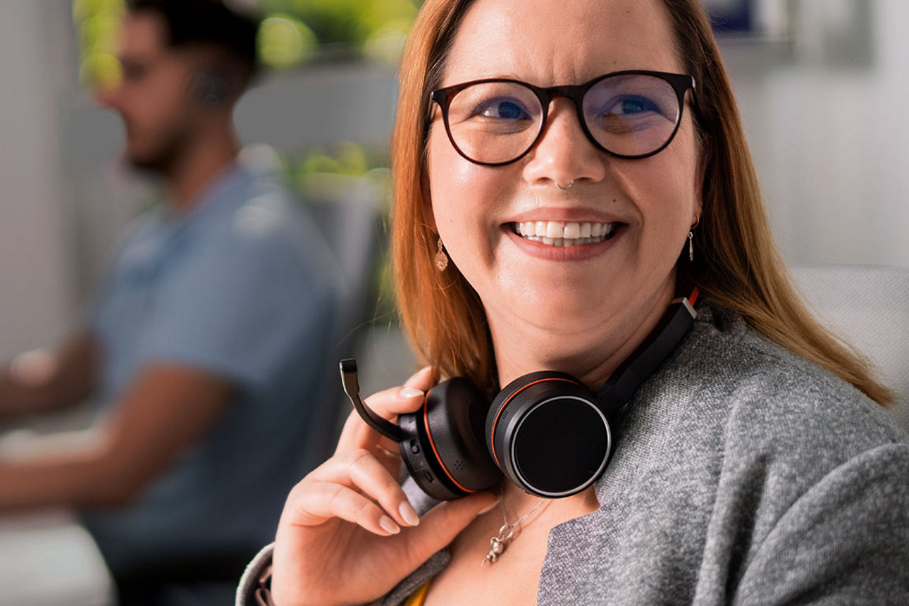 Eine Frau mit Headset sitzt lächelnd an ihrem Arbeitsplatz