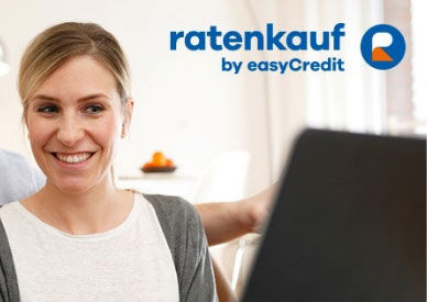 Frau schaut lächelnd auf ein Laptop, plus Text ratenkauf by easyCredit