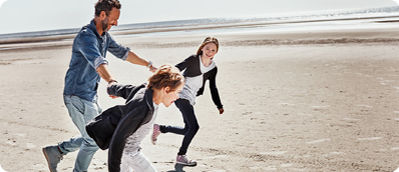 Ein Vater rennt mit seinen Kindern lachend und glücklich am Strand